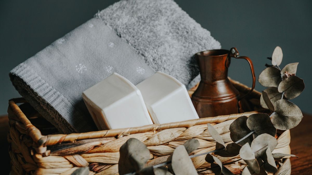 A woven basket holding folded towels, soap bars and dried eucalyptus.
