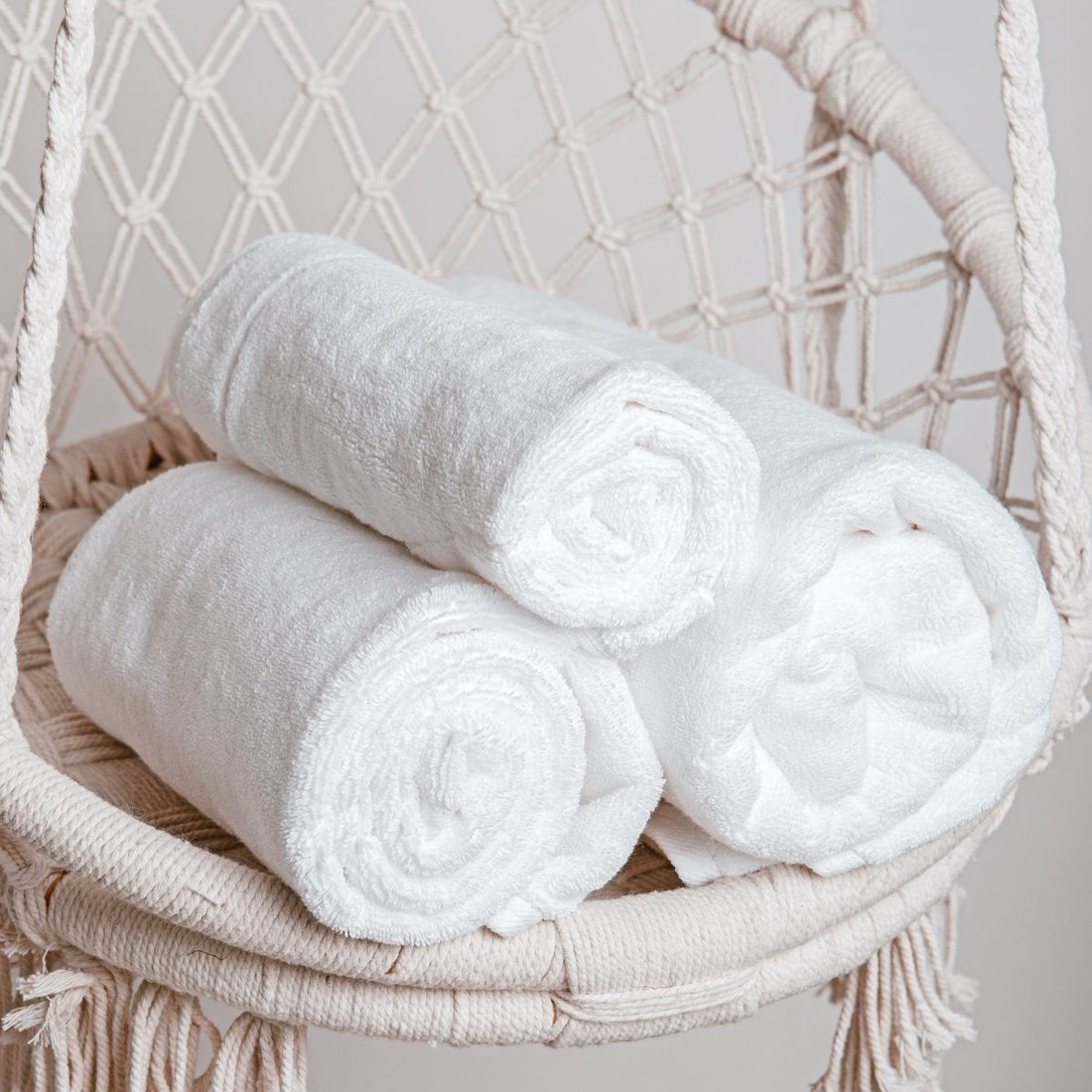 Three rolled white towels resting in a woven hanging chair.