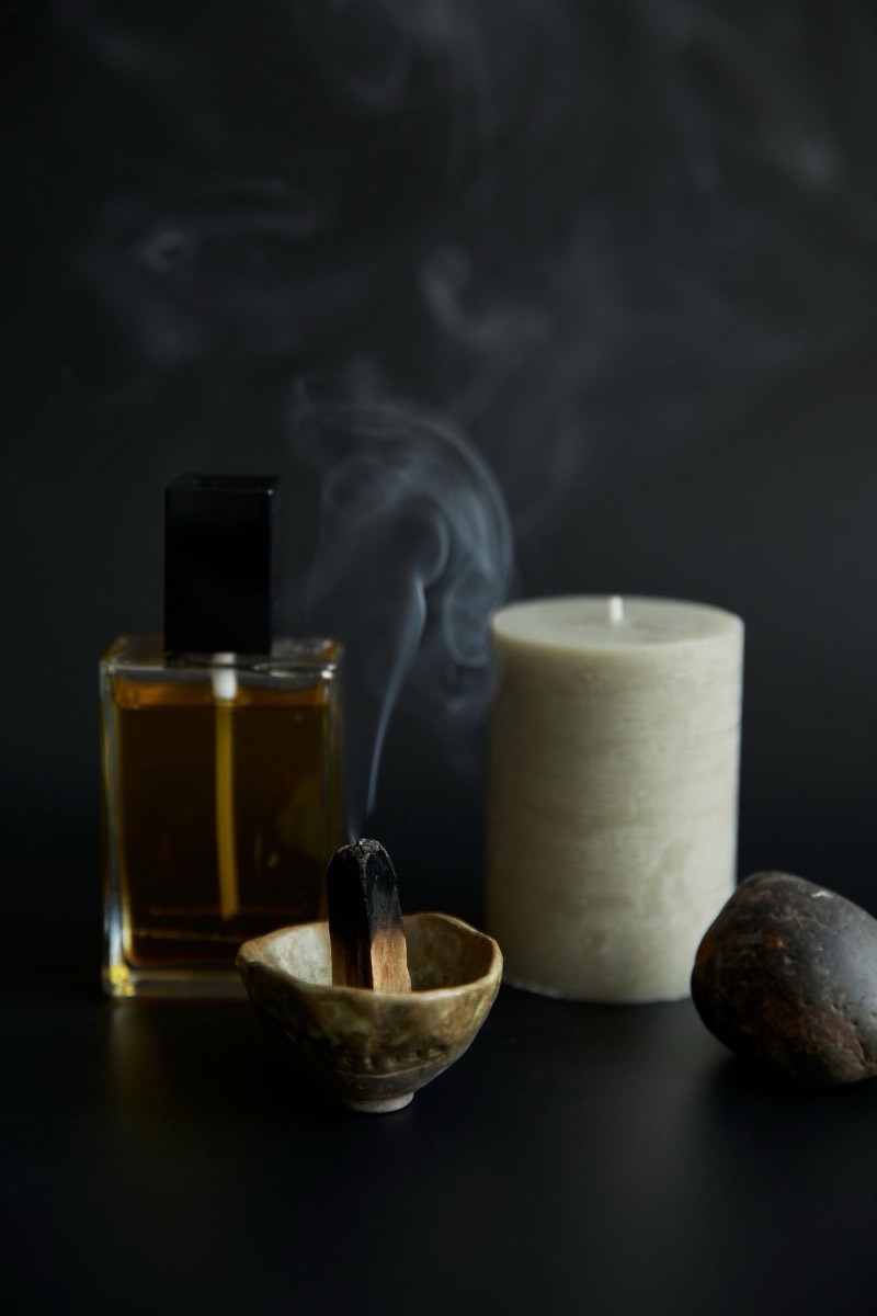 A lit candle, an amber oil bottle and an incense bowl on a dark surface.