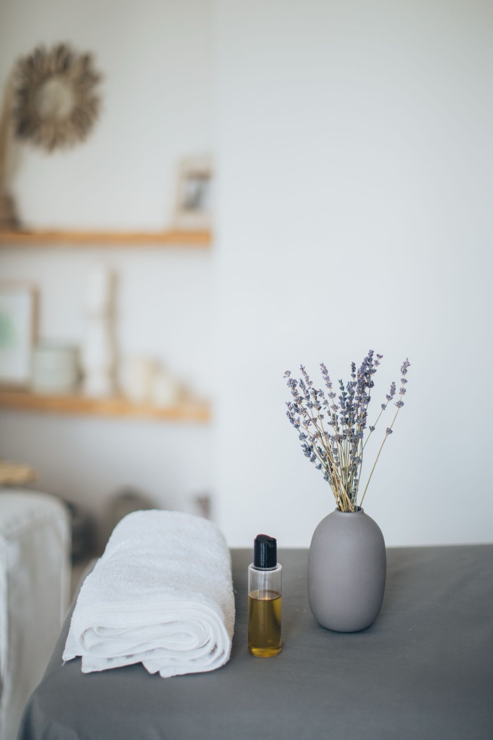 A folded white towel, a small bottle of massage oil and dried lavender on a treatment table.